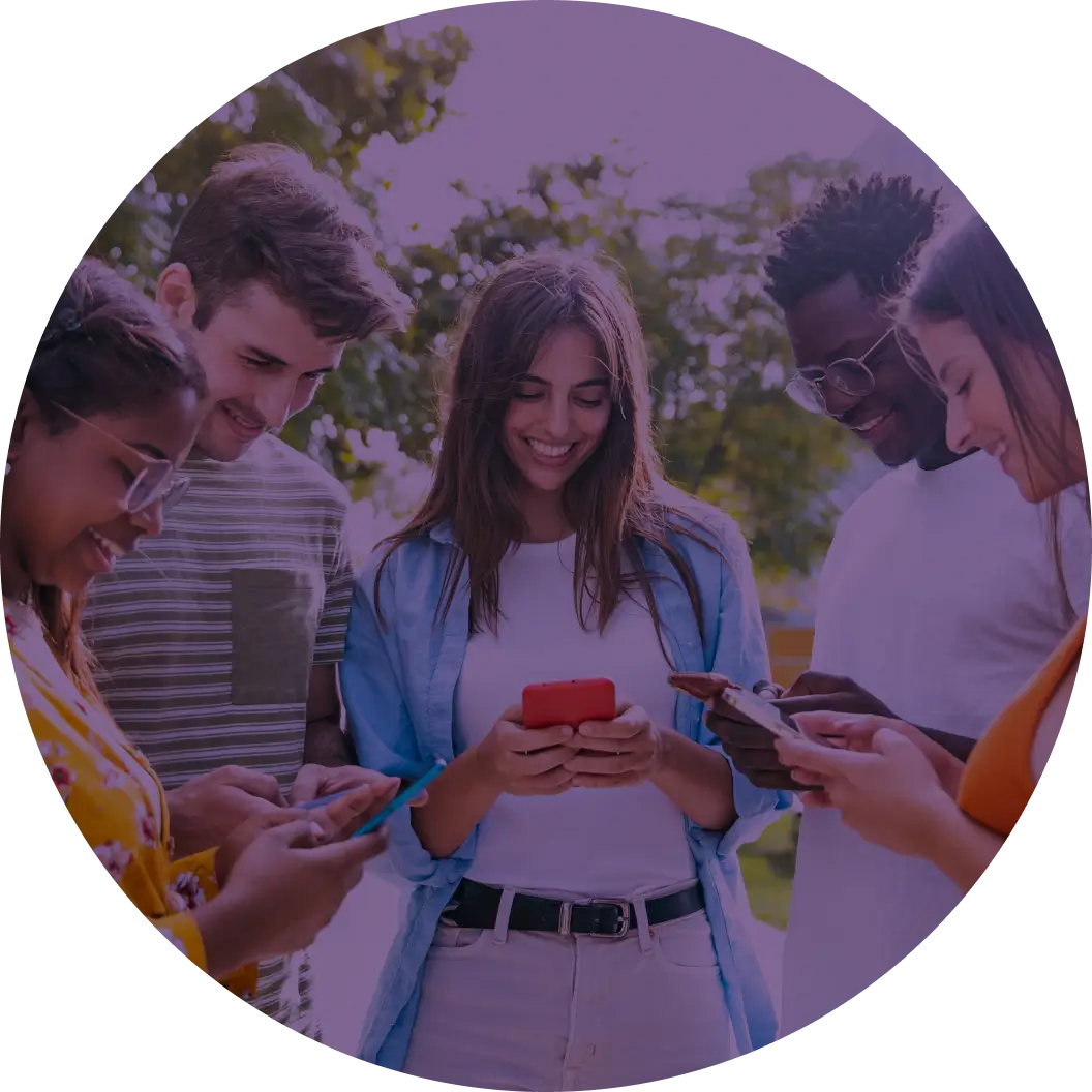 Three people standing together laugh and smile while looking at their phones